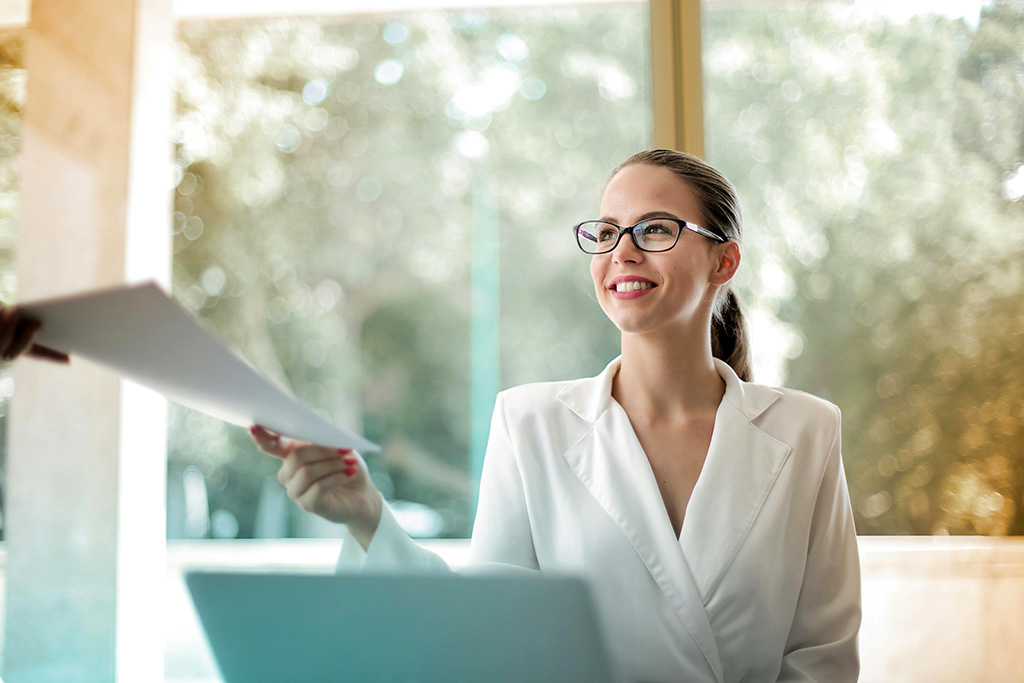 Cheeful office worker handing over paper work at desk