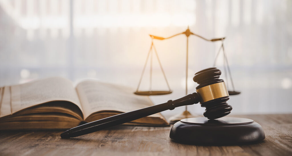 Courtroom gavel placed next to a weight scale and legal book